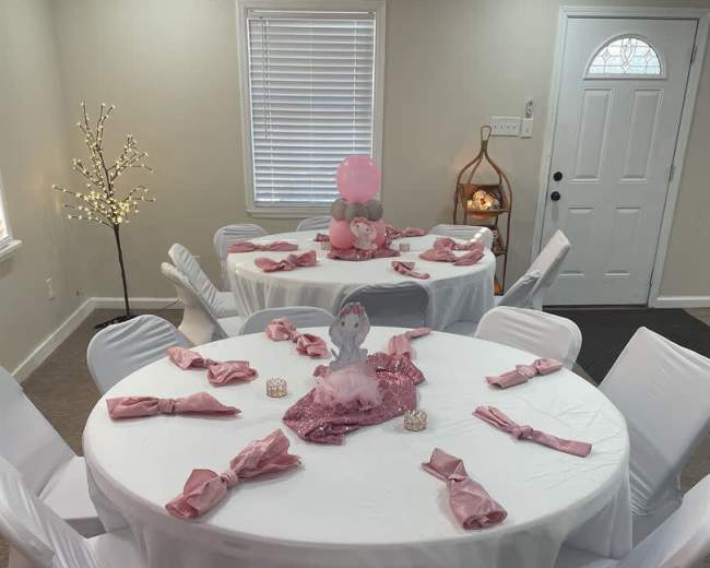 A banquet area with multiple round tables covered in white tablecloths, each set with pink napkins and a decorative centerpiece.