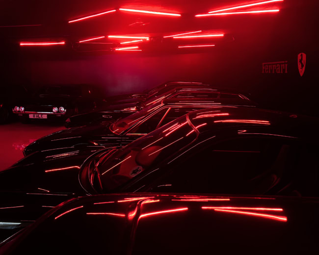 A row of black cars is illuminated by red neon lights in a dark garage.