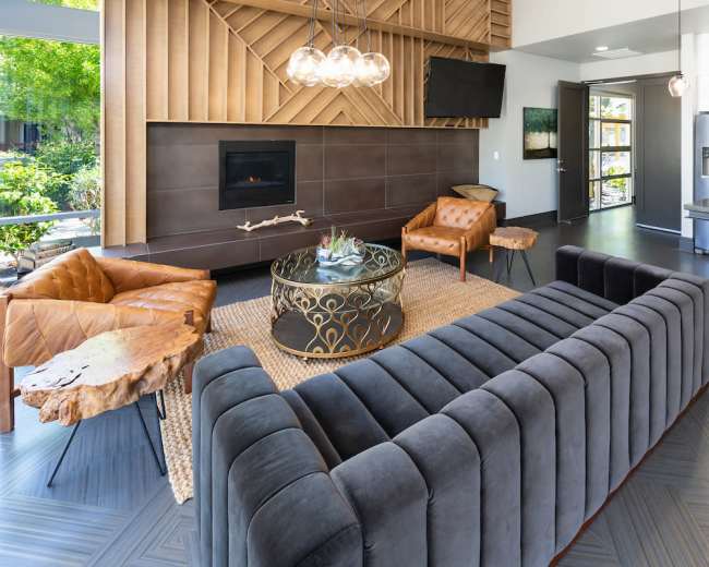 The living area features a modern design with a sectional sofa, leather chairs, a round coffee table, and a fireplace, all accentuated by large windows allowing natural light.