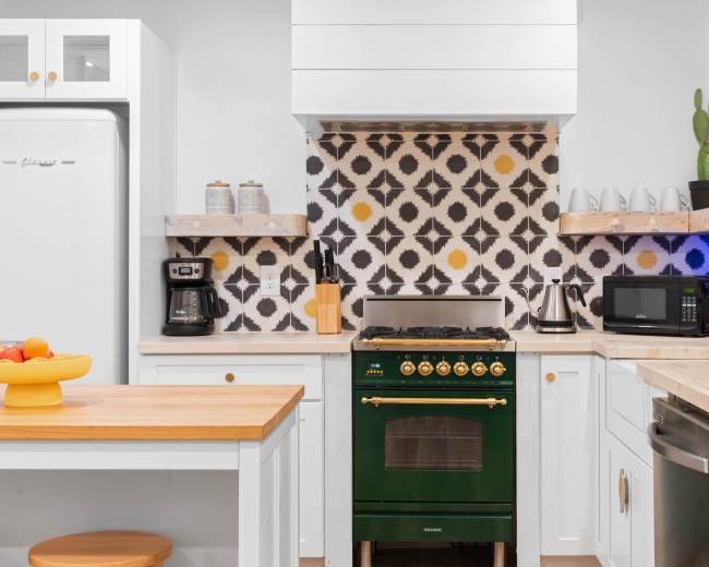A modern kitchen features a green stove, white cabinets, and patterned tile backsplash, with wooden countertops and appliances neatly arranged.