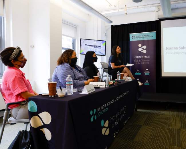 A panel discussion takes place in a conference room, featuring speakers presenting to an audience, while a table with water bottles and coffee cups is positioned in the foreground.