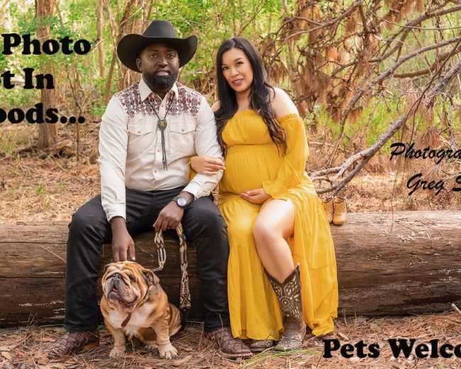 A couple poses on a fallen log in a wooded area, with a bulldog sitting beside them, as they prepare for a family photo shoot.