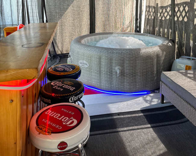 A hot tub sits inside a gazebo with a bar area, surrounded by privacy curtains and string lights.