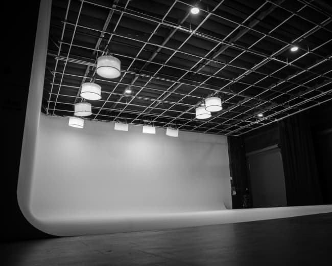 An empty photography studio with a white backdrop and overhead lighting fixtures.