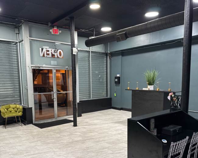 The image shows an empty interior space with gray tiled flooring, a reception area with a black counter, and large glass doors that display "OPEN."
