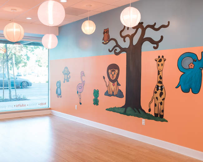 The image shows a brightly colored room featuring a mural with various animal characters on the walls and hanging light fixtures.
