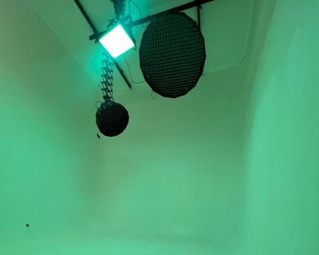 A minimalist studio space with two black lights hanging from the ceiling and green lighting illuminating the white walls.