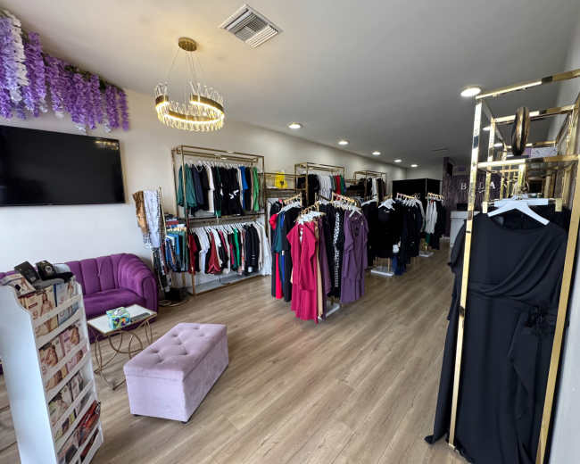 The image shows a clothing store interior with racks of colorful garments, a purple sofa, and a chandelier.