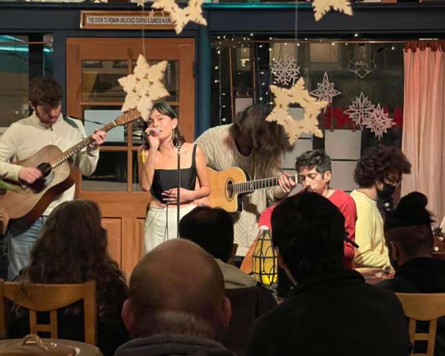 A group of musicians performs on stage in a cozy café while an audience watches attentively.