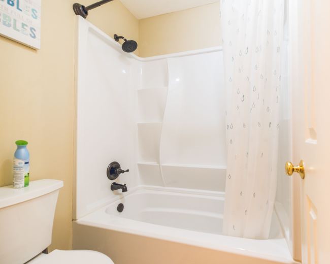 The image shows a bathroom with a shower-tub combination, a toilet, and a shower curtain.