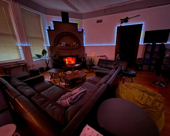 The image shows a cozy living room with a fireplace surrounded by dark furniture and soft lighting, including LED strips along the walls.