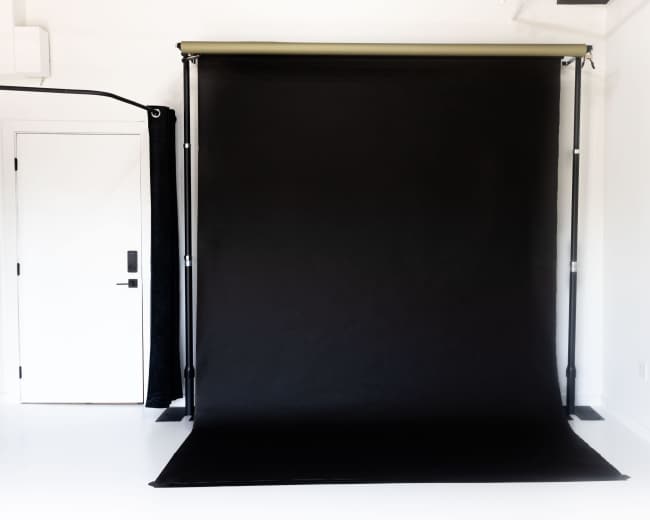The image shows a black photography backdrop set up against a white wall in a studio space.