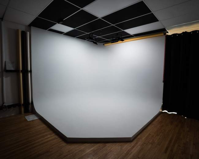 The image shows a photography studio with a seamless white backdrop and a wooden floor.