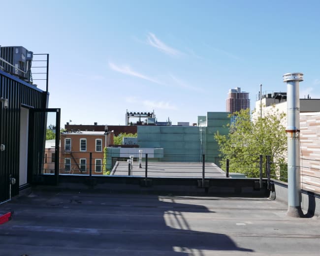 The image shows a flat rooftop with various cooling units, adjacent buildings, and a clear blue sky.