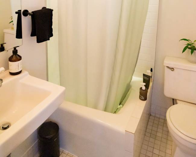 The image shows a small bathroom featuring a shower with a light green curtain, a white sink, and a toilet.