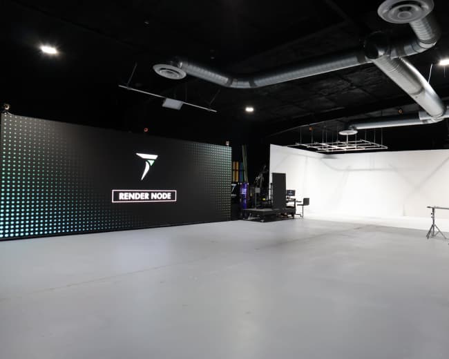 The image shows an empty studio space with a large digital display on the left and a blank white backdrop on the right, equipped with studio equipment and lighting setups.