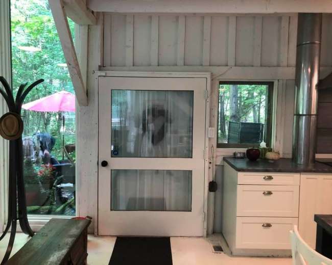 A light-colored door with a glass panel is visible, leading to an outdoor area surrounded by greenery and patio furniture.