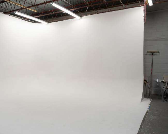 An empty photography studio with a seamless white backdrop and overhead lighting.