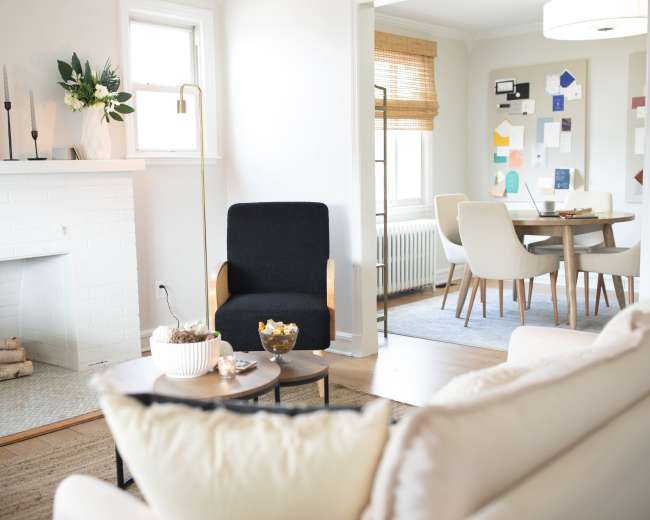 The image features a modern living room with a black accent chair, a white fireplace, and a dining area visible in the background.