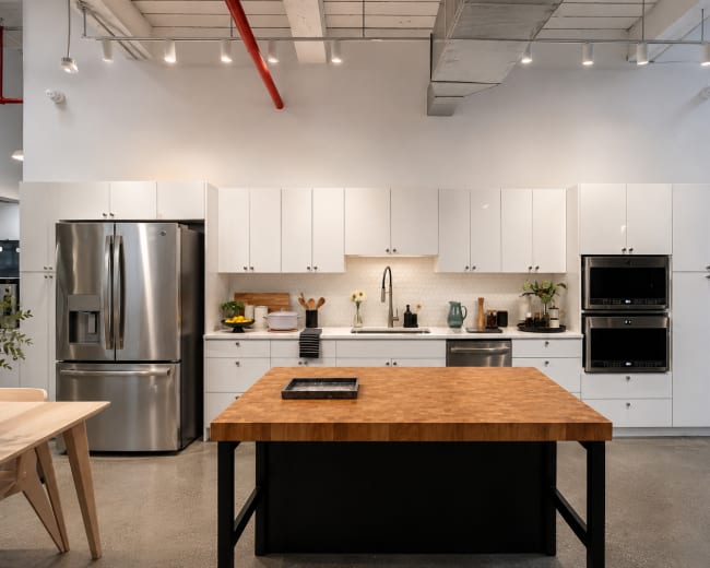 The image shows a modern kitchen featuring white cabinetry, a stainless steel refrigerator, and a central wooden island with a black base.