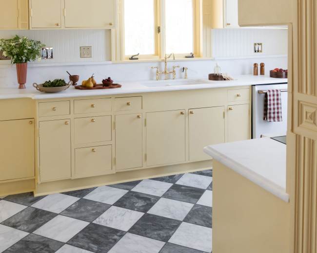 The image shows a bright kitchen featuring yellow cabinetry, a marble countertop, and a checkered floor.