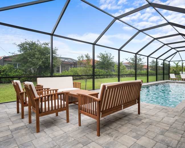 A screened patio area with wooden furniture surrounding a rectangular swimming pool.