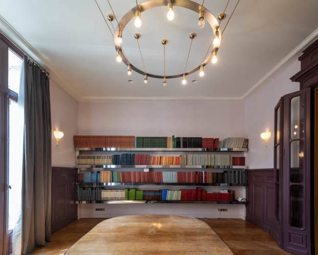 A well-lit room features a circular light fixture hanging from the ceiling and shelves filled with neatly arranged books along the walls.