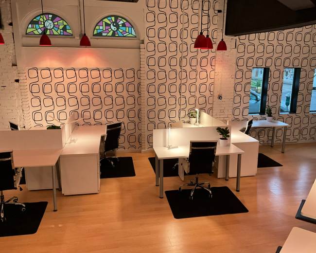 The image shows a modern office space with white desks and chairs, accented by patterned wallpaper and colorful pendant lights.