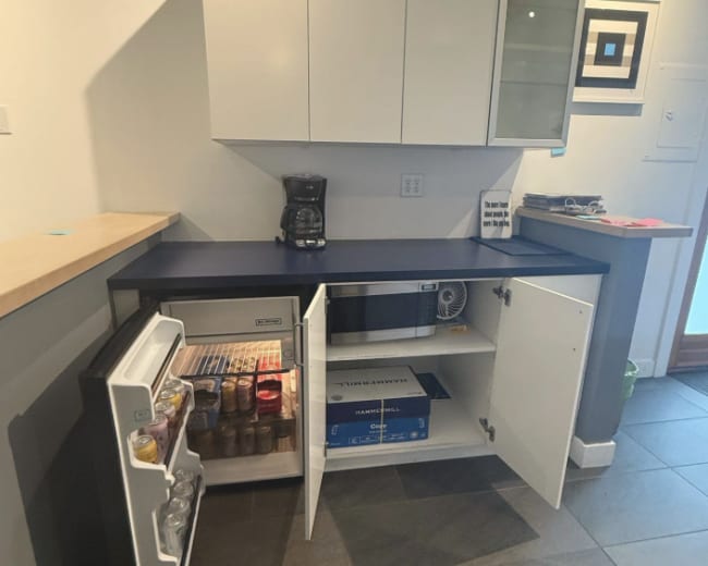 The image shows a modern kitchen corner with a refrigerator and upper cabinets, featuring an open freezer and a coffee maker on the counter.