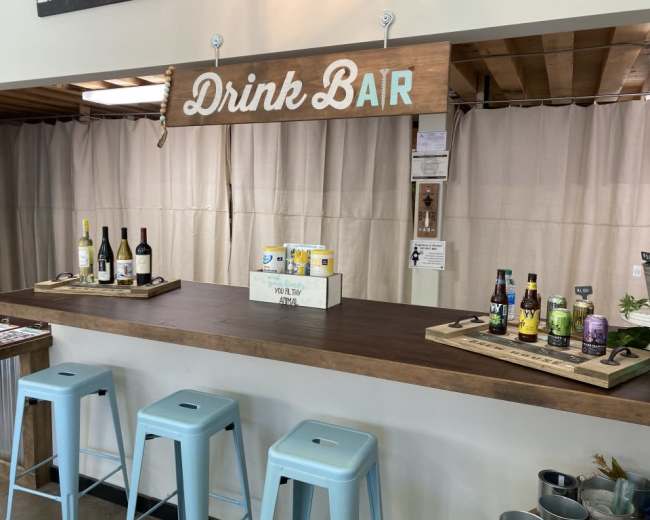 A drink bar with various bottles of wine and craft beverages displayed on wooden trays, under a sign that reads "Drink Bar."
