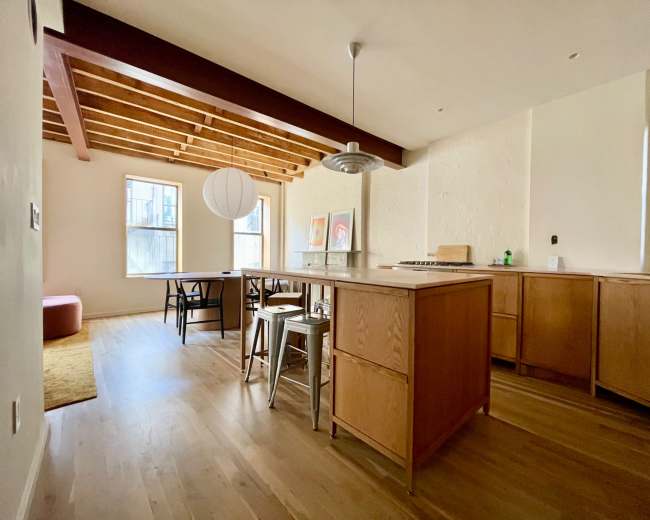 The image shows a modern kitchen and dining area with wooden beams, a central island, and a dining table surrounded by chairs.