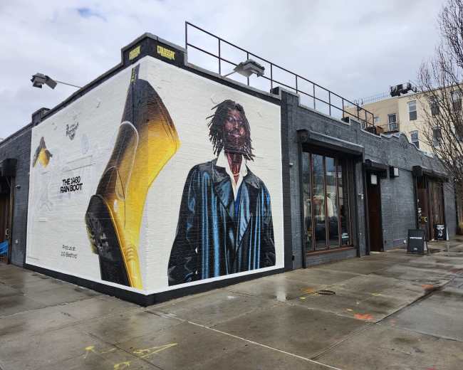 The image shows a building with a large mural depicting a figure dressed in a suit on one side, set against a gray sky.