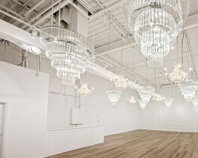 The image shows a spacious room with multiple crystal chandeliers hanging from the ceiling and wooden flooring.