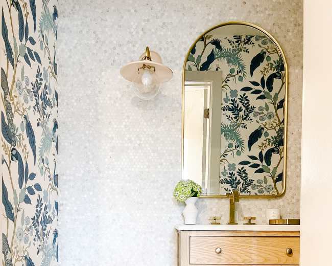 A bathroom featuring a wooden vanity with a mirror, floral-patterned wallpaper, and a light fixture.