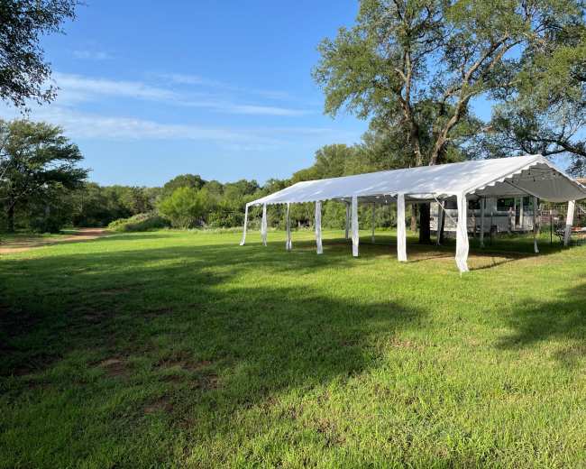 A large white tent is set up on a grassy area surrounded by trees and open fields.