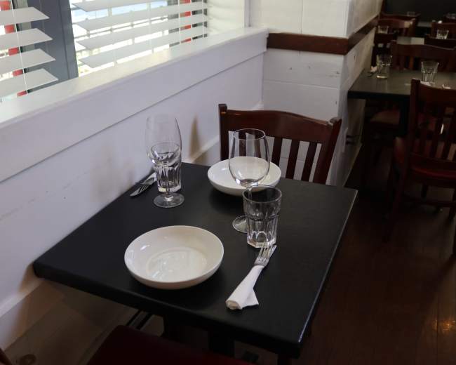 A table set for two in a restaurant features white plates, glasses, and utensils.