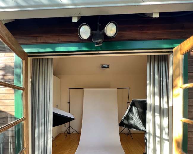 A photo studio with a plain backdrop and multiple softbox lights set up, visible through open double doors.