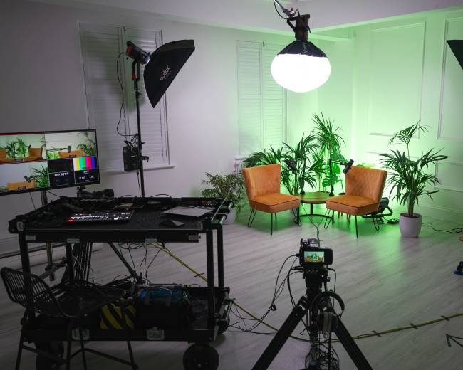 A well-equipped photo studio features two orange chairs, bright lighting, and various pieces of filming equipment arranged around the space.