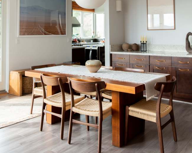 A dining area features a wooden table surrounded by chairs, with a large pendant light above and a sideboard against the wall.