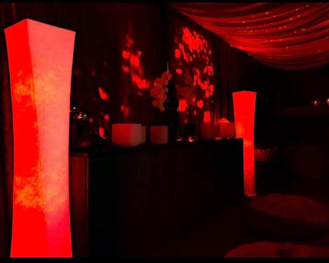 A dimly lit room with red illuminated columns, decorative candles, and soft textures in the background.