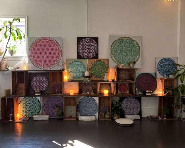 The image shows a display of decorative circular mandalas arranged on wooden shelves, illuminated by soft lighting in a serene interior space.