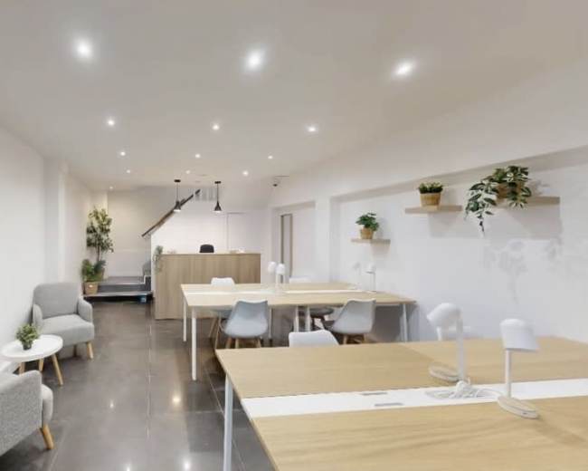 The image shows a modern office space with several tables, chairs, and potted plants, featuring bright overhead lighting and a clean, minimalistic design.