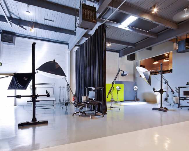A spacious photography studio with various lighting setups, a chair, and a backdrop curtain.