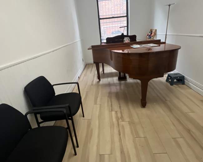 The image shows a minimalistic office space featuring a wooden desk, two black chairs, and a window allowing natural light.