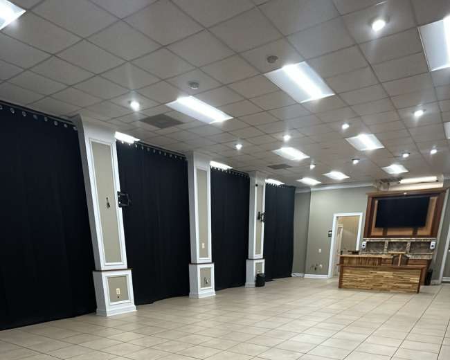 A spacious room with tiled flooring, black curtains on the walls, and a wooden structure at the far end.