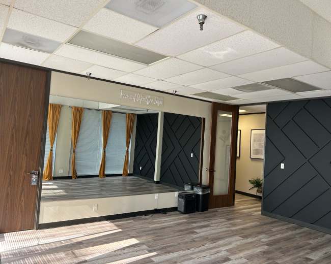 The image shows a well-lit room featuring a large mirror, decorative wall panels, and large windows with yellow curtains.