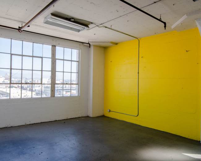 A bright yellow wall contrasts with the white walls in a spacious room with large windows overlooking a cityscape.