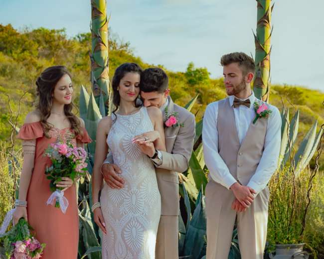 A bride and groom stand together at an outdoor wedding altar, flanked by two attendants holding bouquets.