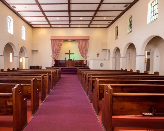 The interior of a church featuring pews arranged in rows facing a raised altar with a cross at the front.