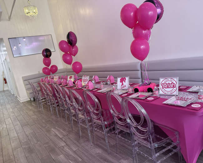 A long, elegantly set party table is adorned with pink decorations, balloons, and themed party supplies.